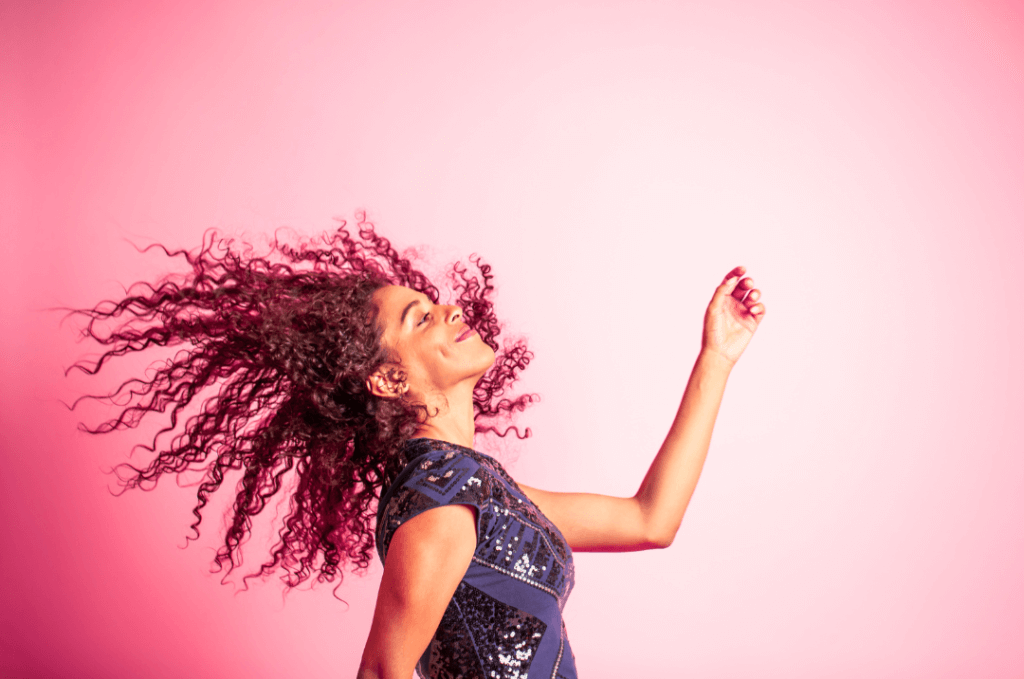 Joyful woman dancing with her hair flying, set against a vibrant pink background for the Move and Groove challenge.